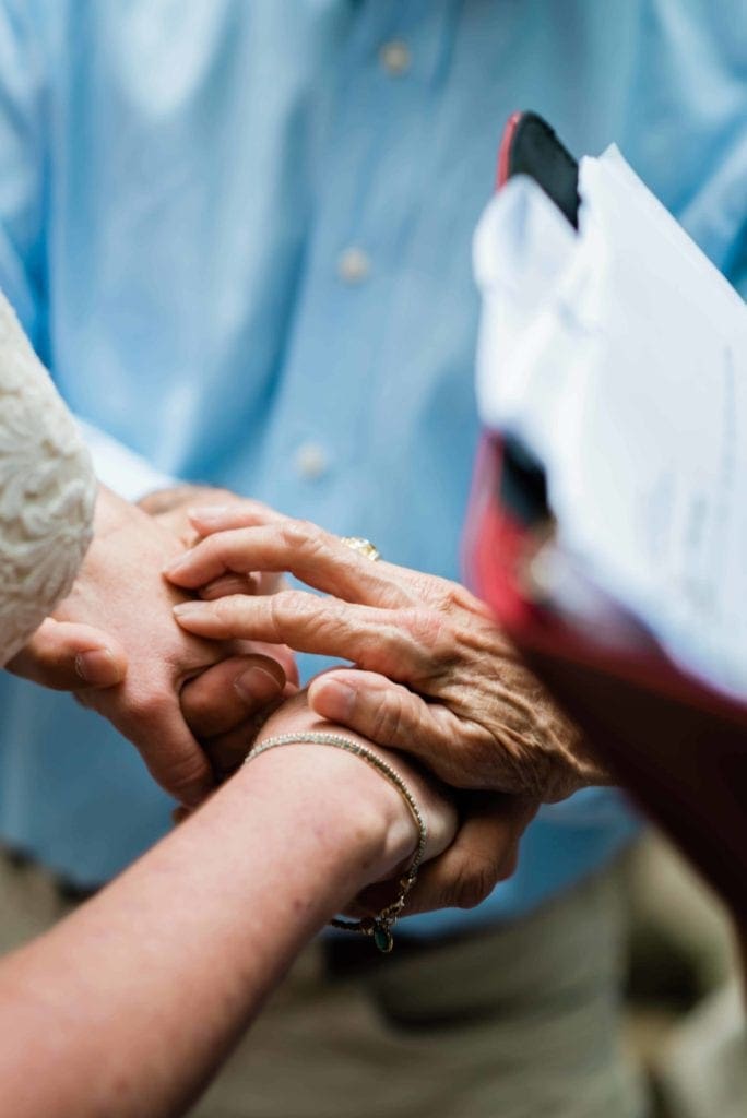 in an intimate adventure elopement with family, the image is a close up of the mother's hand covers the bride and grooms hands while she performs the ceremony as their officiant.