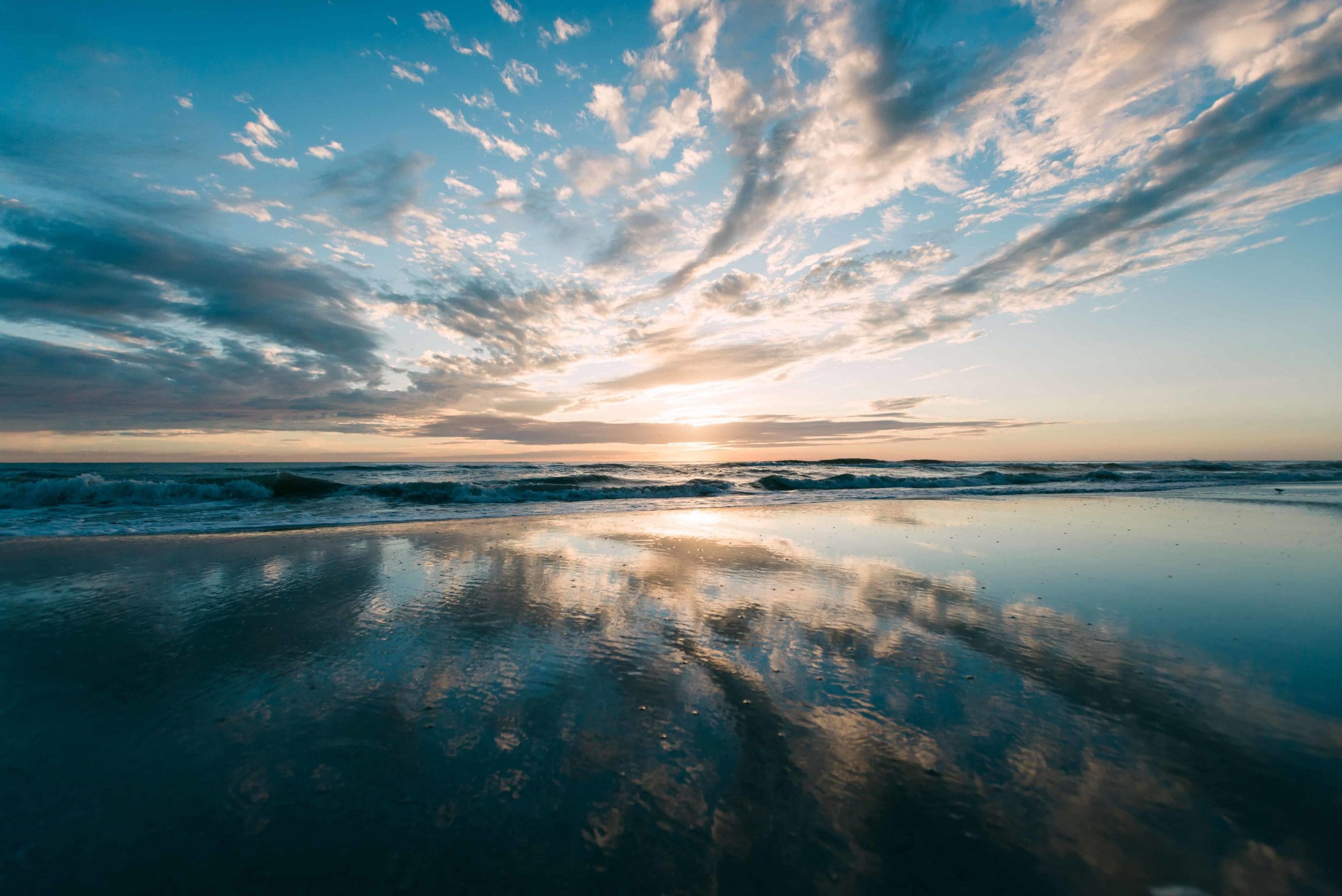 This is a picture of the beach in Florida. The sky is vast, blue, with some small clouds. The sand is reflecting the sky almost perfectly. There are waves in the ocean. This would be the best place to elope in florida on an adventure elopement package