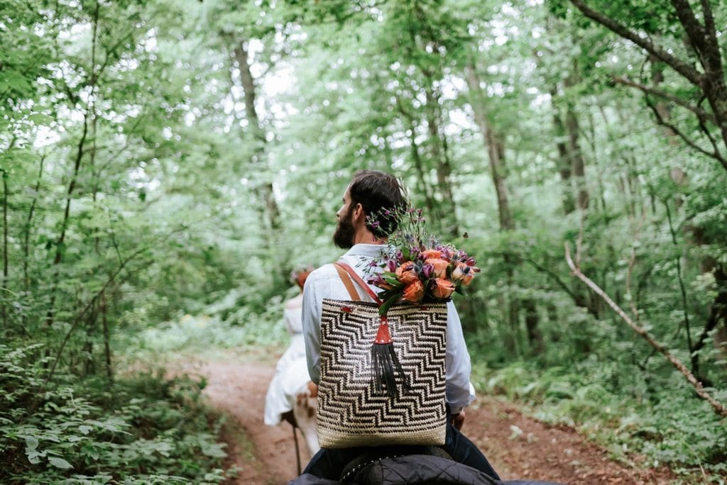 This is a picture of a bride and groom on horseback following their guide while horsebackriding in the woods.