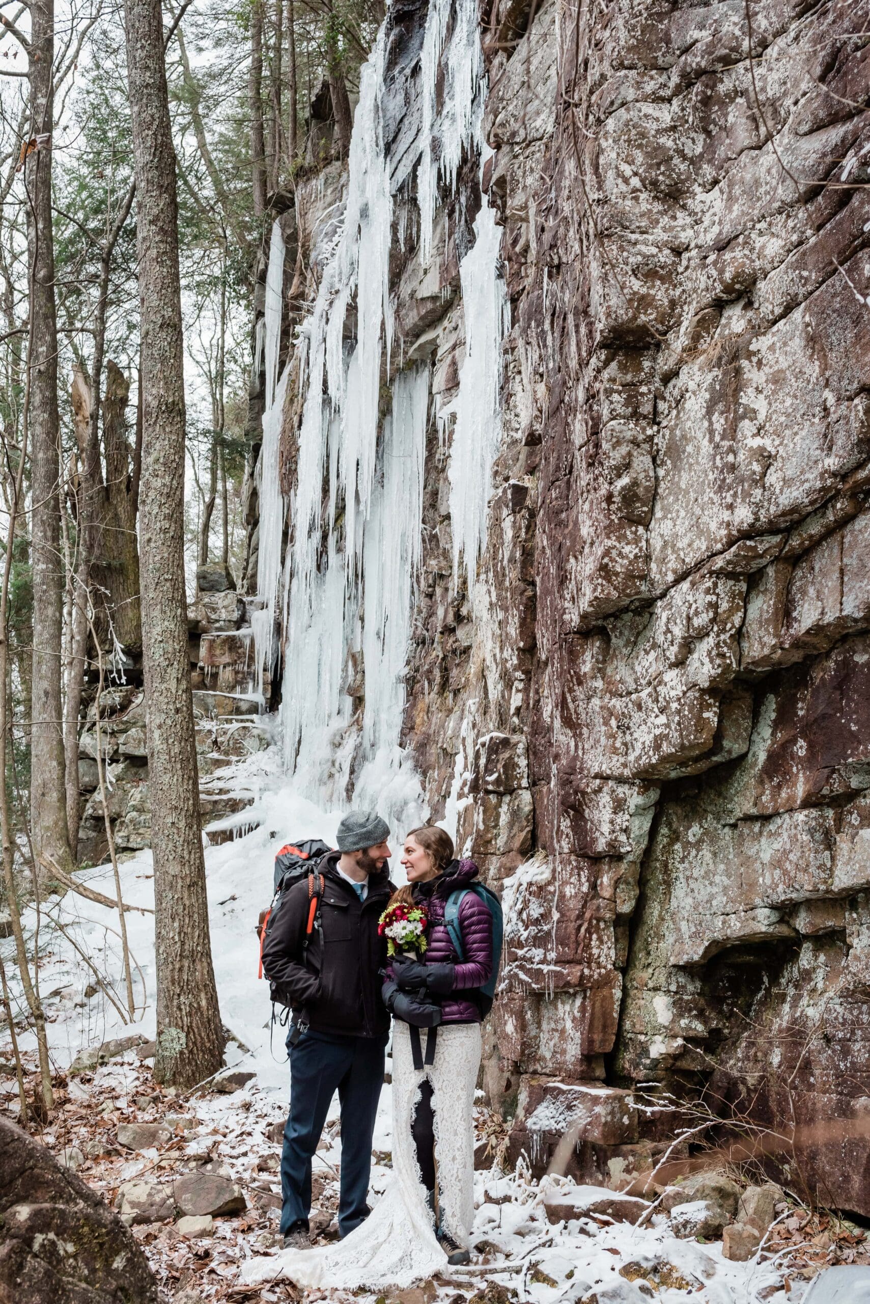 This is a winter Chattanooga elopement. This picture is the bride and groom bundled up in the snowy forest next to a ice covered wall where they had hoped to climbing