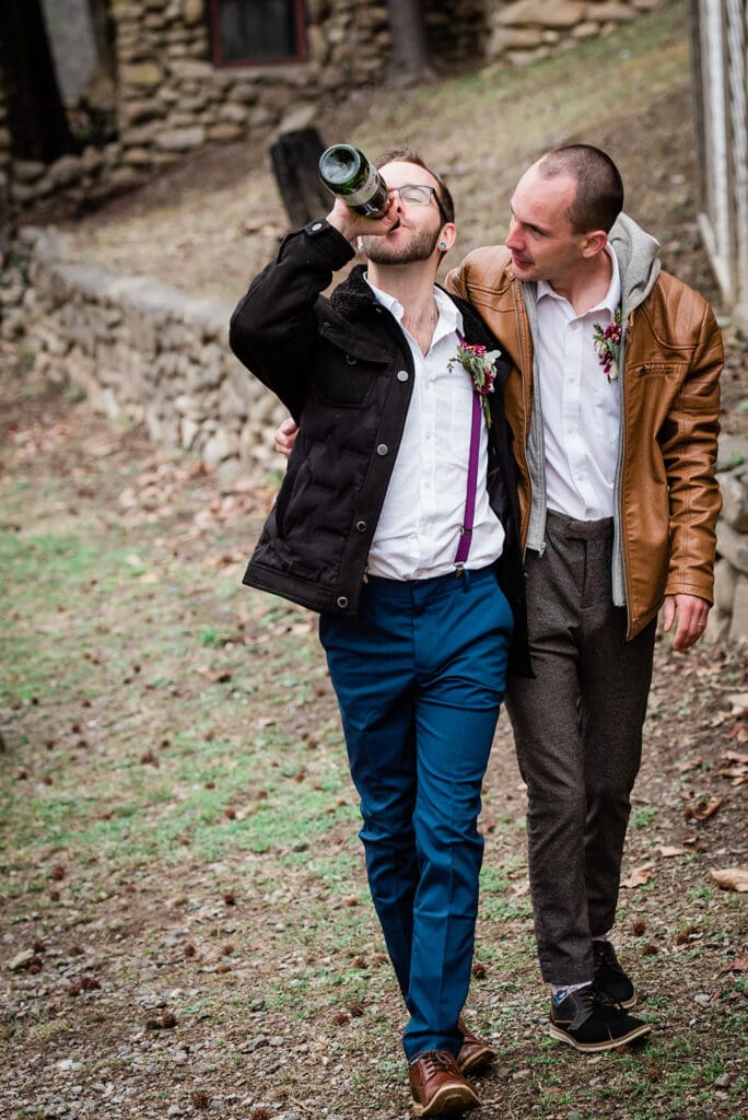 This is a picture of two men walking down a path together. They are drinking champagne out of the bottle together.