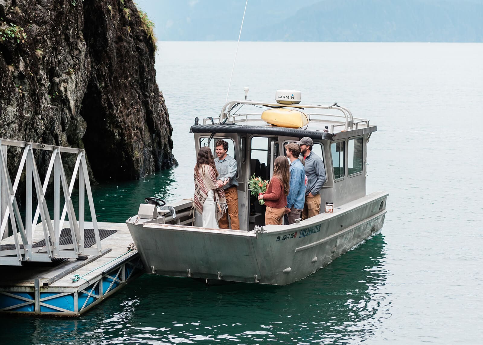 This is a picture of a bride and groom standing on a boat with their loved ones during their Alaska destination elopement with family.