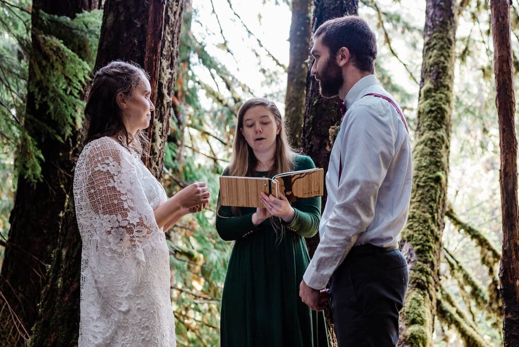 An officiant does a reading during a private elopement ceremony in an old growth temperate rainforest as part of a multi-day adventure elopement experience