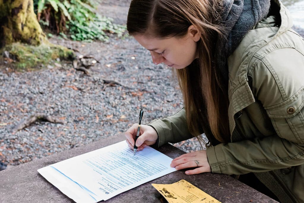 An officiant signs the marriage license after a private elopement ceremony in an old growth temperate rainforest as part of a multi-day adventure elopement experience