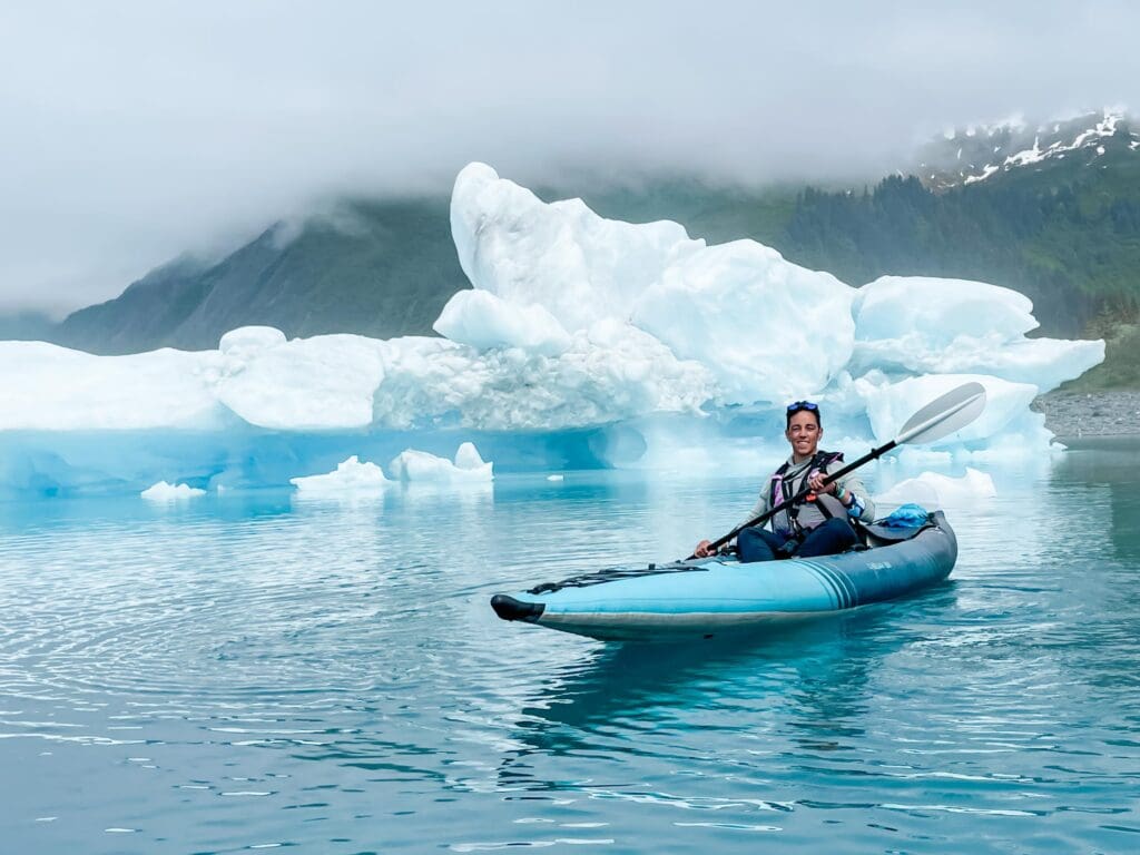 Alaska elopement photographer and planner Kate Okenatez-Mahoney, sits in a kayak as she paddles between icebergs in the Bear Glacier Lagoon in Alaska.