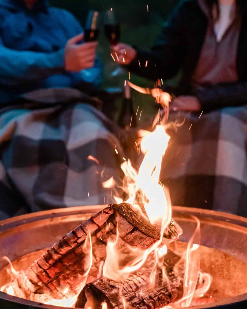 Over a crackling campfire at glamping near Juneau, Alaska, a couple snuggles under a wool blanket the night of their adventurous luxury glacier elopement in Alaska.