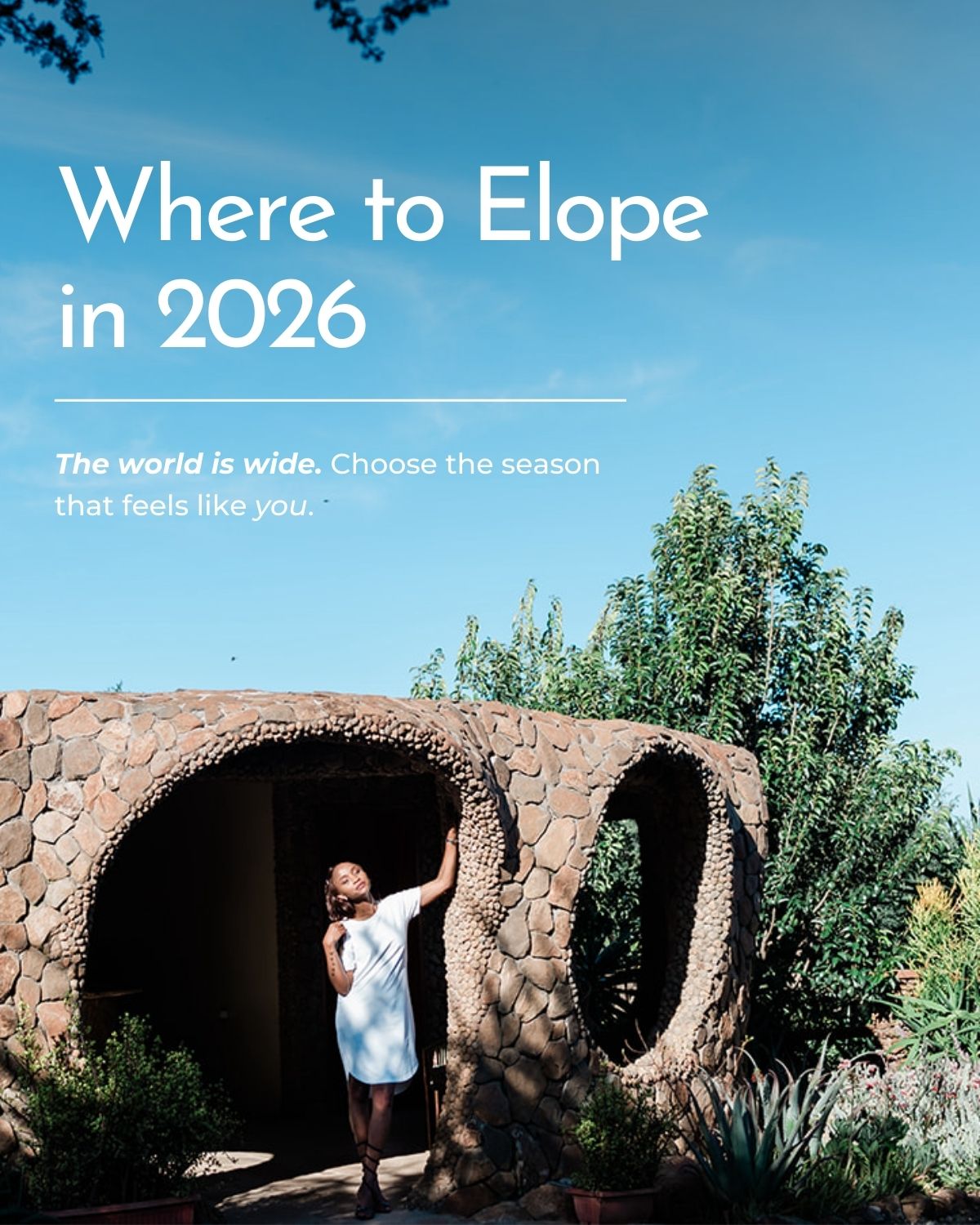 A bride stands, leaning against an interesting stone building, that is round in shape with round windows in the Rift Valley in Keyna during her international luxury elopement. She gazes thoughtfully into the lens of the camera.