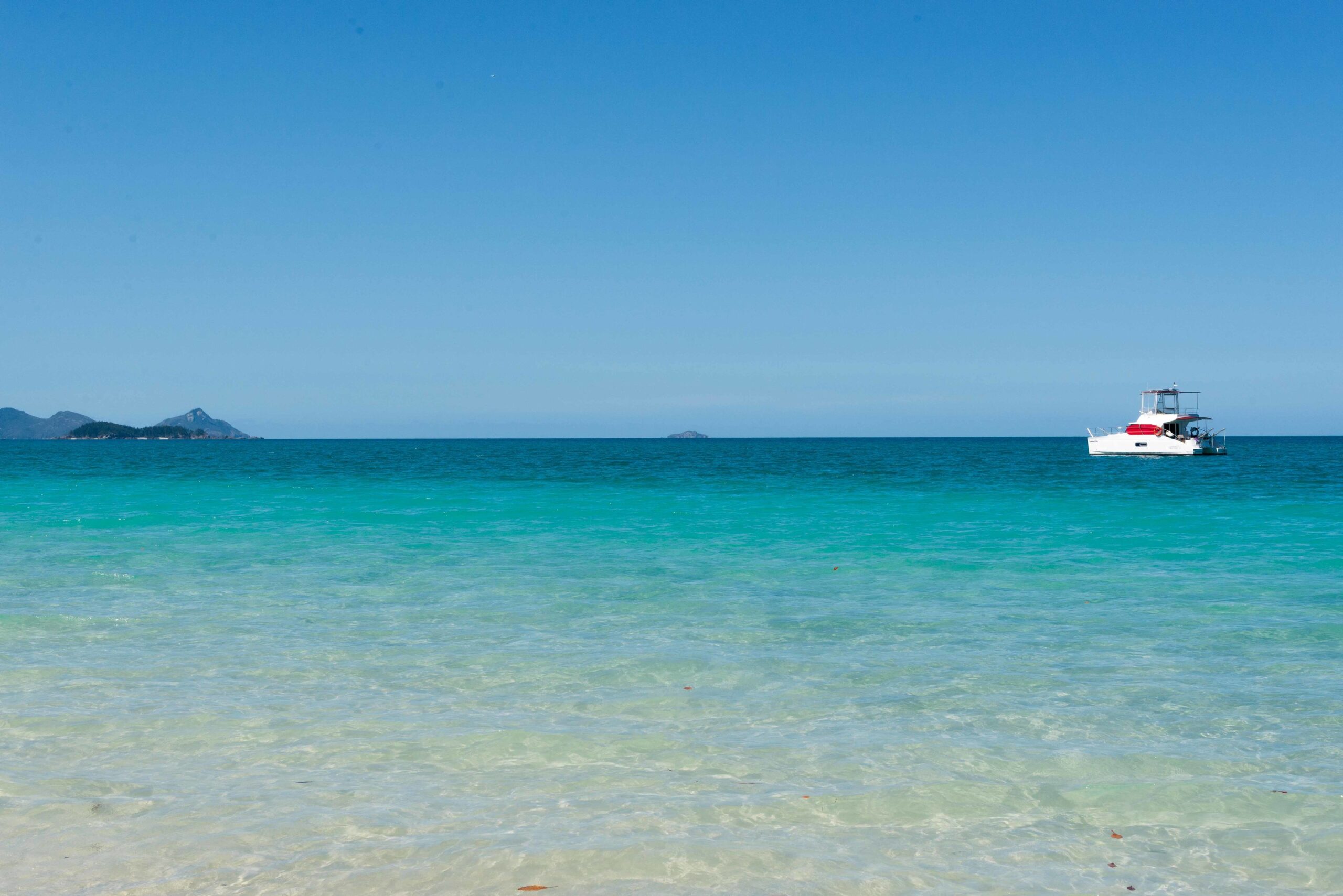 a white and red accented catamaran yacht in Australia in the distance surrounded by blue sky and turquoise blue water. during an immersive adventure luxe elopement experienced designed by Soul & Sky Weddings