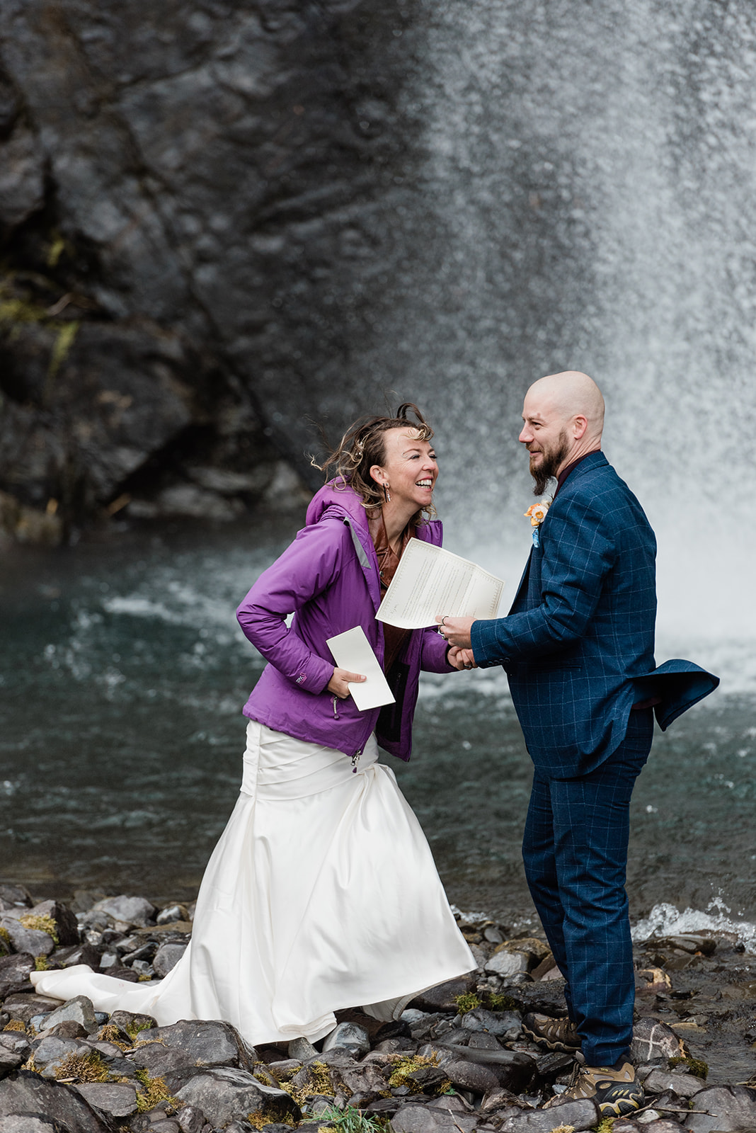 This is a picture of an elopement by a waterfall. It is the bride and groom happy and reading their vows.