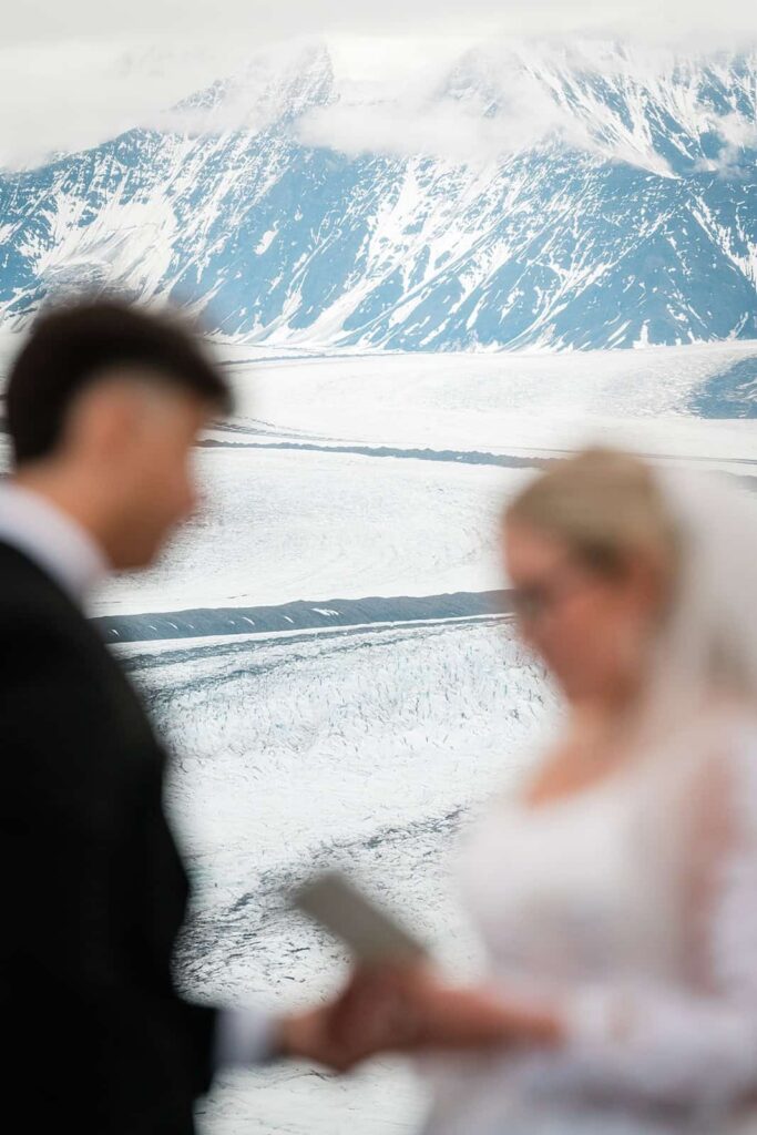 This picture is of an alaskan elopement, the bride and groom are saying their vows. Behind them, you can see the Matanuska glacier with mountainous terrain filling the back of the frame.