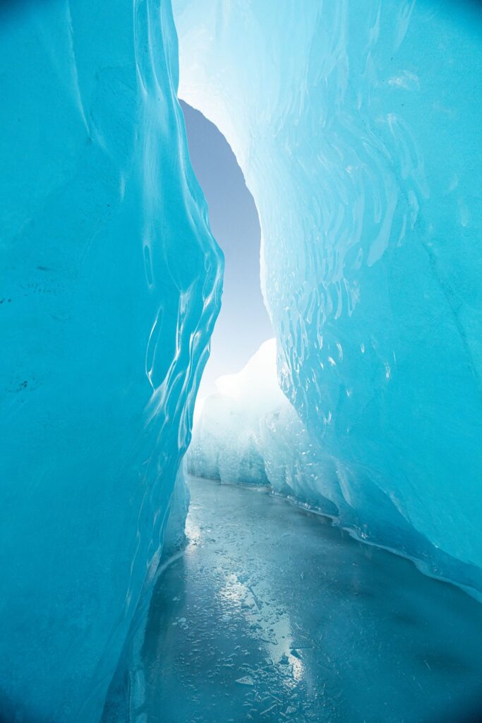 The image is of a Knik glacier ice cave in the winter during a helicopter elopement.  There blue sky out the end of the cave, with the bright blue ice on either side.