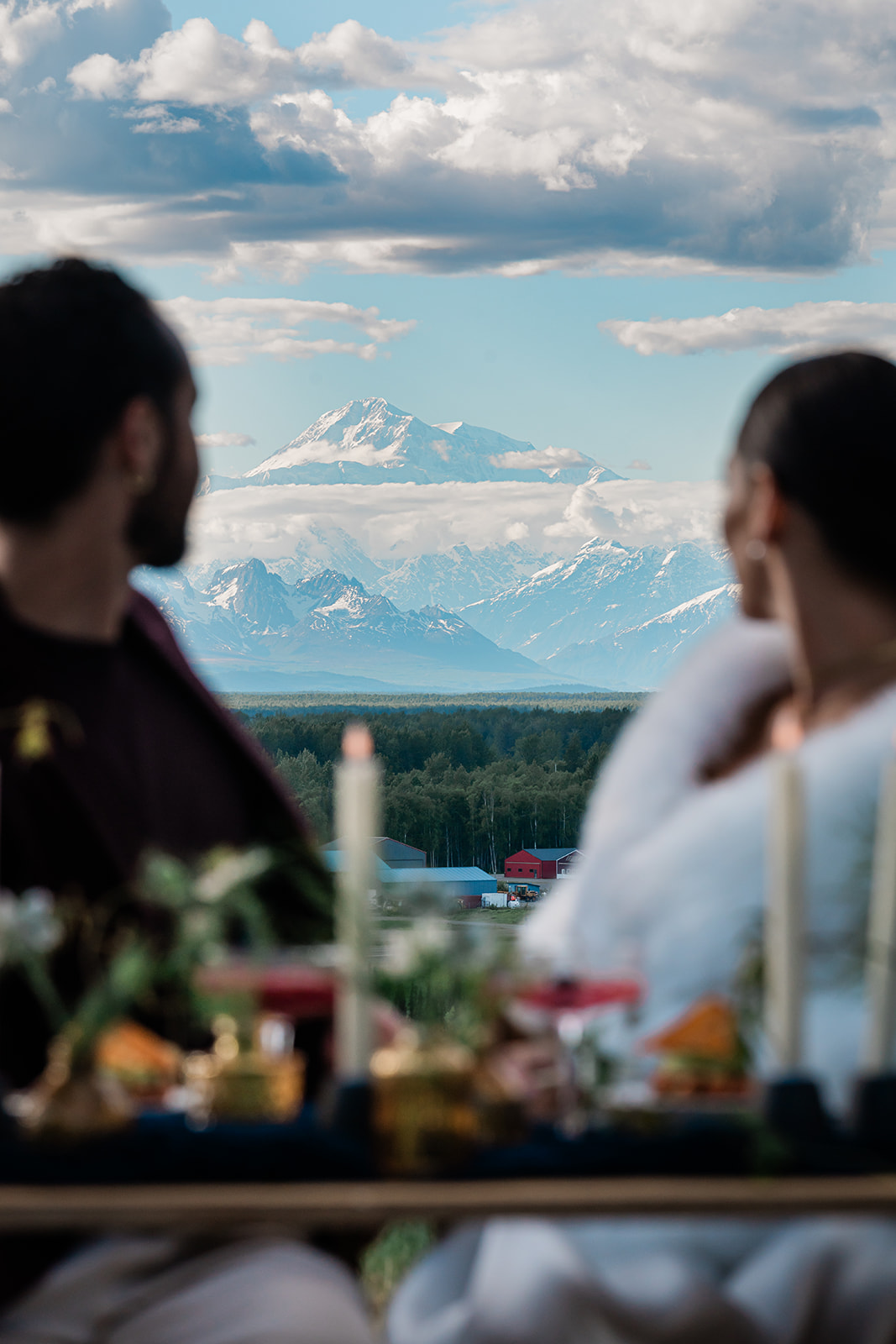 This picture is of a bride and groom looking behind them to the hulking shape of Denali Mountain after their elopement day on Ruth Glacier. They are having a private dinner and the sweetheart table is set with candles, and other luxury, romantic touches.