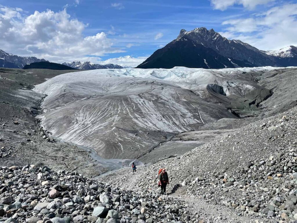 This is a picture of an elopement crew hiking on Root Glacier. Behind you see a giant mountain and the glacier landscape.