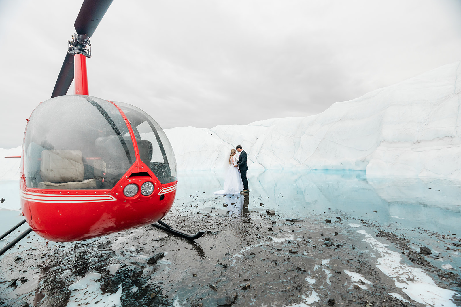 A couple exchanges vows beside a bright blue glacier pool on the Matanuska Glacier, their helicopter waiting nearby on the ice.